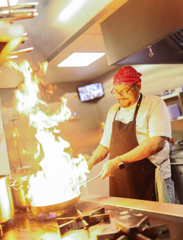 A chef crafting an Indian dish theatrically with flames coming from the pan.
